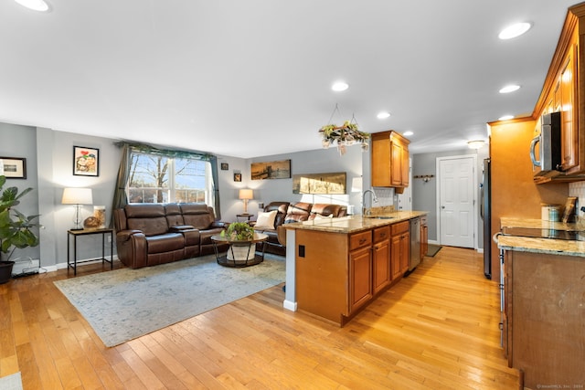 kitchen with sink, light hardwood / wood-style floors, light stone counters, kitchen peninsula, and stainless steel appliances