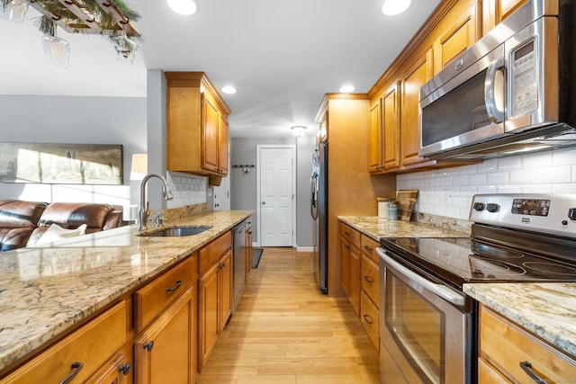 kitchen with light stone countertops, light wood-type flooring, backsplash, stainless steel appliances, and sink