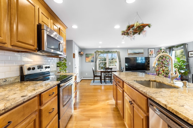 kitchen with light stone counters, light wood-type flooring, sink, and appliances with stainless steel finishes