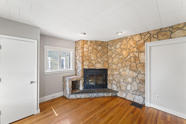 unfurnished living room with hardwood / wood-style flooring and a stone fireplace