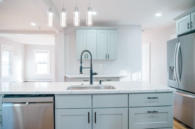 kitchen featuring light stone counters, light wood-style flooring, a sink, appliances with stainless steel finishes, and decorative light fixtures