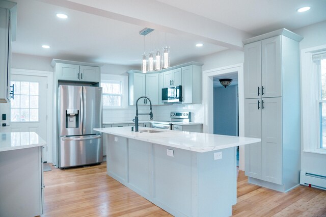 kitchen featuring appliances with stainless steel finishes, light hardwood / wood-style flooring, hanging light fixtures, and a kitchen island with sink