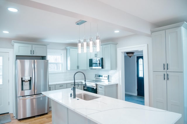 kitchen with a kitchen island with sink, a sink, appliances with stainless steel finishes, decorative backsplash, and decorative light fixtures