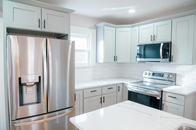 kitchen with tasteful backsplash, light stone countertops, white cabinetry, and appliances with stainless steel finishes