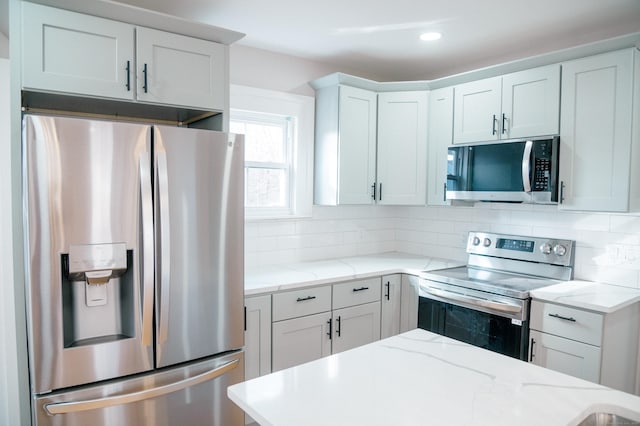 kitchen with stainless steel appliances, tasteful backsplash, white cabinets, and light stone countertops