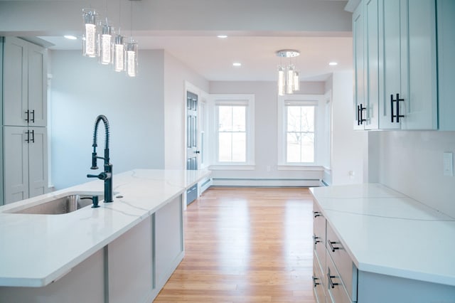 kitchen with light wood-style floors, a baseboard heating unit, a sink, and decorative light fixtures