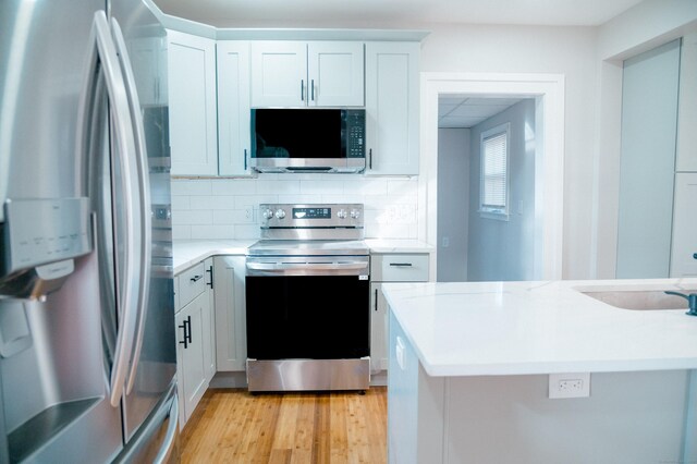 kitchen with sink, light hardwood / wood-style flooring, decorative backsplash, white cabinetry, and stainless steel appliances