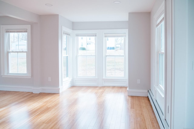 empty room with a baseboard radiator, light wood-style flooring, and baseboards