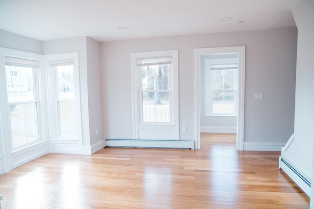 empty room featuring a baseboard heating unit, light wood-type flooring, baseboards, and baseboard heating