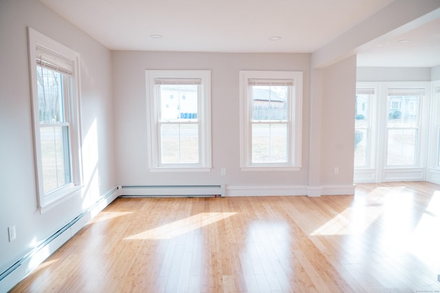 unfurnished room featuring a baseboard heating unit, light wood-type flooring, and baseboards