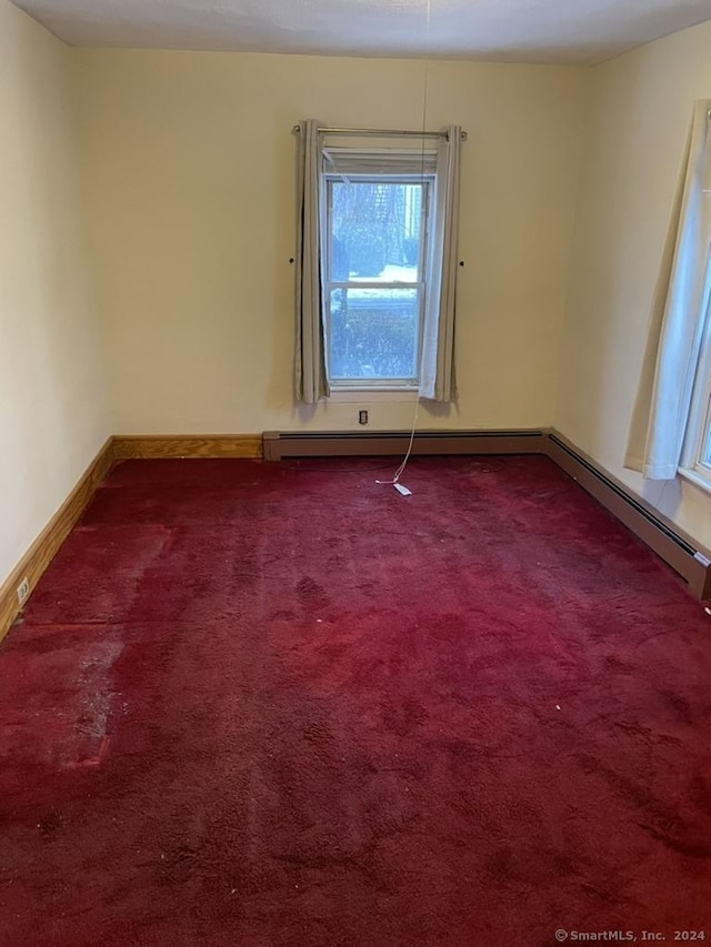 carpeted spare room with a baseboard heating unit