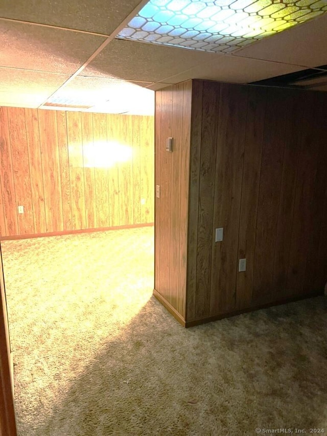 basement featuring a drop ceiling, carpet floors, and wooden walls