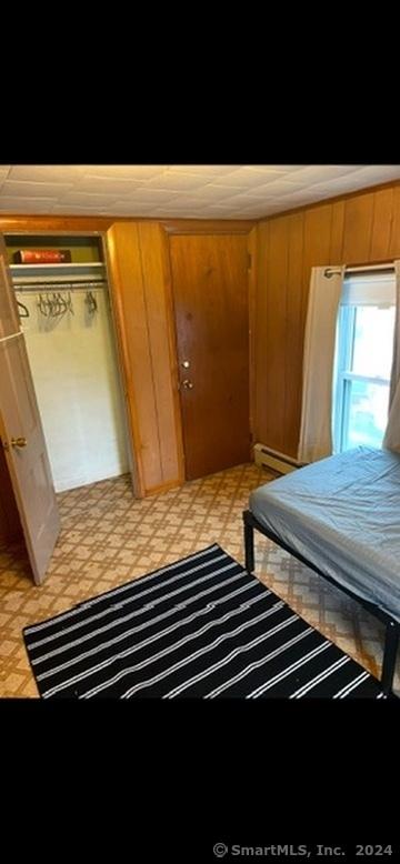 bedroom with wood walls, a closet, and a baseboard heating unit