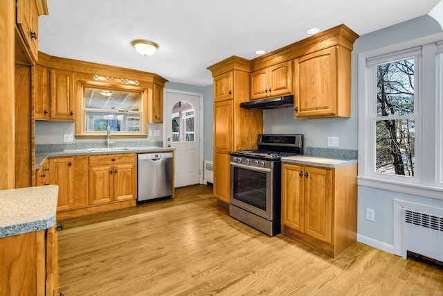 kitchen with radiator heating unit, sink, stainless steel appliances, plenty of natural light, and light wood-type flooring