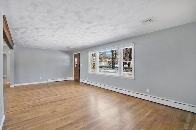 empty room featuring a textured ceiling, light wood-type flooring, and baseboard heating