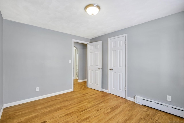 unfurnished bedroom with baseboard heating, a closet, and light wood-type flooring