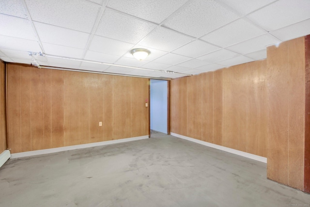 unfurnished room with a paneled ceiling, concrete floors, and wood walls