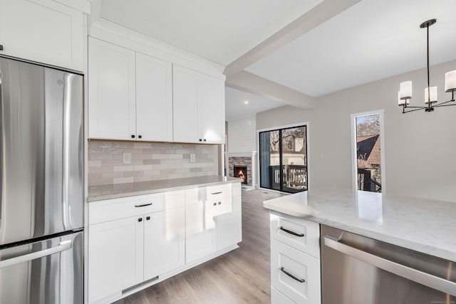 kitchen with decorative backsplash, appliances with stainless steel finishes, white cabinets, pendant lighting, and a fireplace