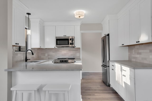 kitchen with decorative backsplash, a peninsula, light countertops, a sink, and stainless steel appliances