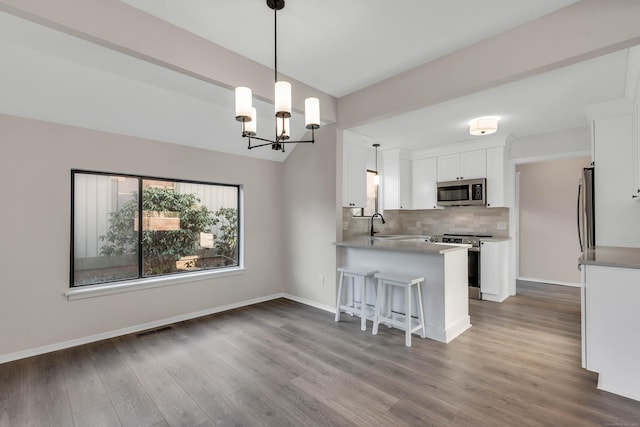 kitchen featuring kitchen peninsula, stainless steel appliances, decorative light fixtures, an inviting chandelier, and white cabinets