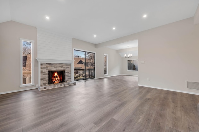 unfurnished living room with hardwood / wood-style flooring, a notable chandelier, vaulted ceiling, and a brick fireplace