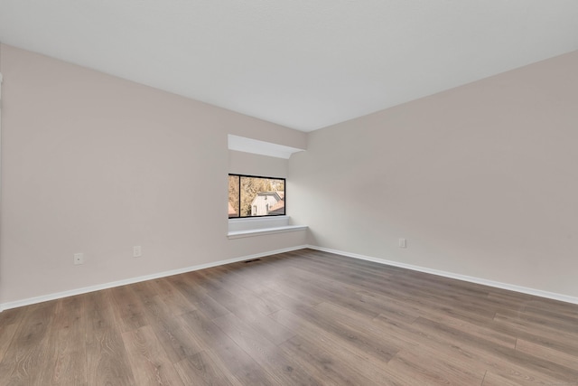 empty room featuring baseboards, wood finished floors, and visible vents