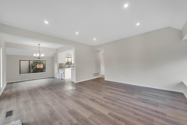 unfurnished living room with light hardwood / wood-style flooring, vaulted ceiling, and a notable chandelier