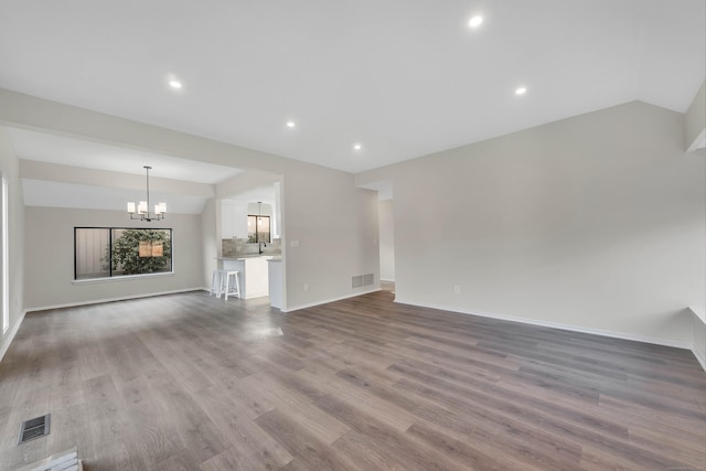 unfurnished living room featuring wood finished floors, vaulted ceiling, a chandelier, and visible vents