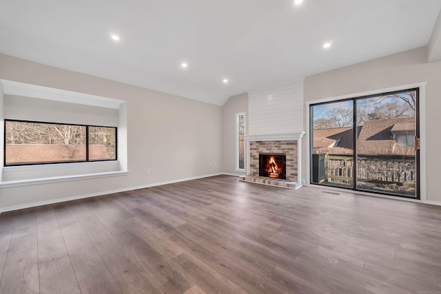 unfurnished living room with baseboards, a fireplace, vaulted ceiling, and wood finished floors