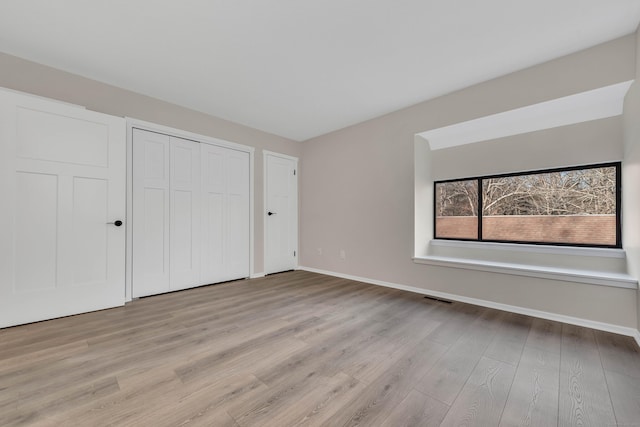 unfurnished bedroom with baseboards, visible vents, light wood-style flooring, and a closet