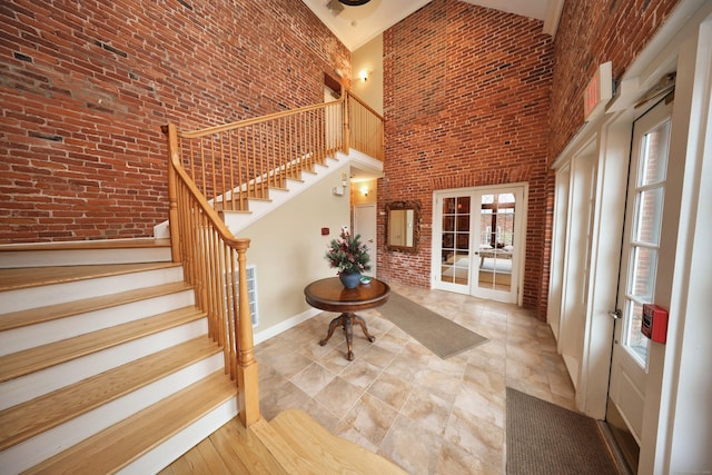 entryway featuring french doors, a towering ceiling, and brick wall