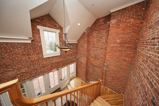 stairs featuring wood-type flooring, vaulted ceiling, and brick wall