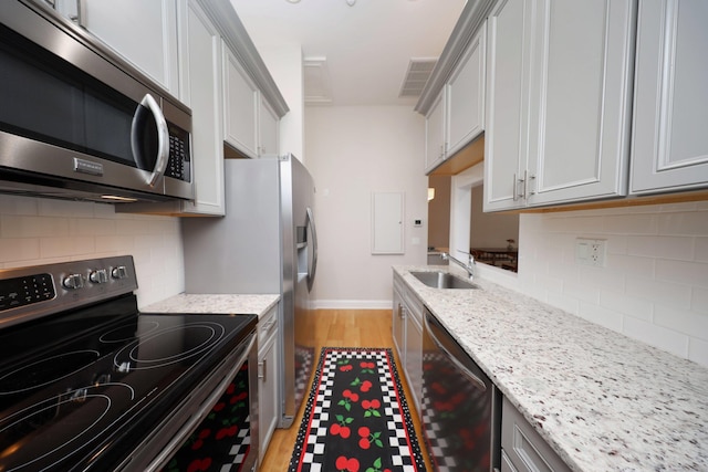 kitchen featuring light stone countertops, sink, stainless steel appliances, tasteful backsplash, and light wood-type flooring