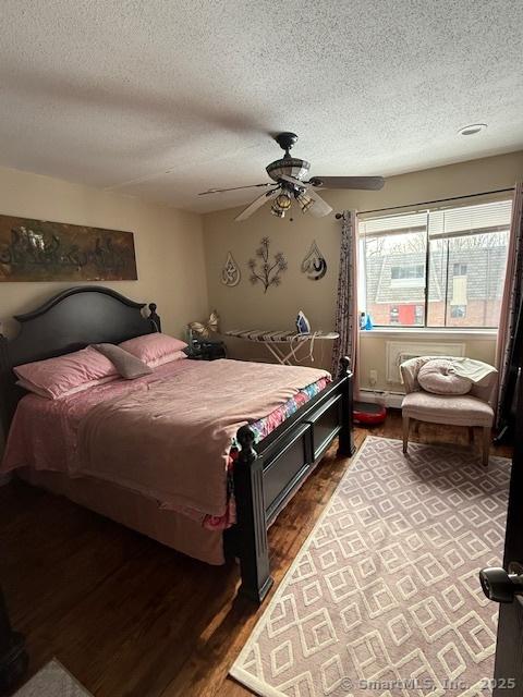 bedroom with a ceiling fan, a baseboard heating unit, a textured ceiling, and wood finished floors