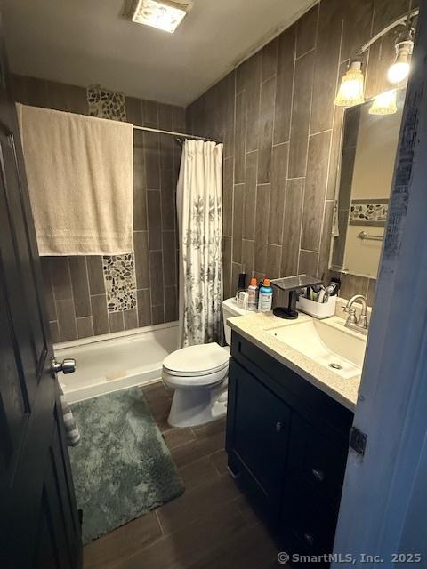 bathroom featuring toilet, wood finish floors, vanity, tile walls, and a shower stall