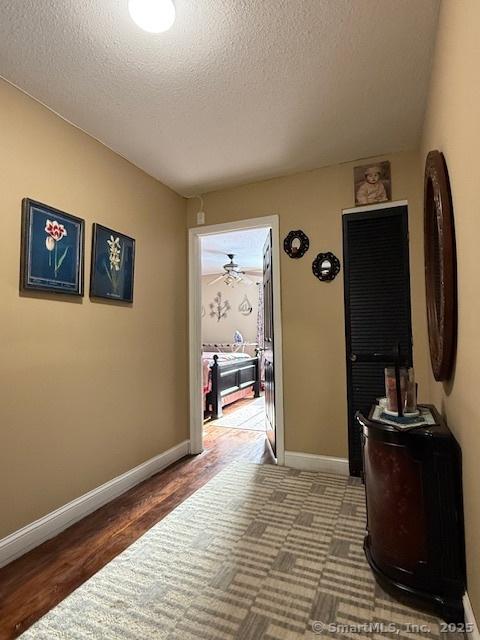 corridor featuring a textured ceiling, wood finished floors, and baseboards