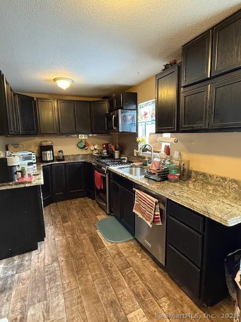 kitchen with wood-type flooring, a textured ceiling, stainless steel appliances, and a sink