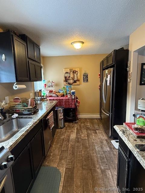 kitchen featuring dark wood-style floors, freestanding refrigerator, a sink, a textured ceiling, and baseboards