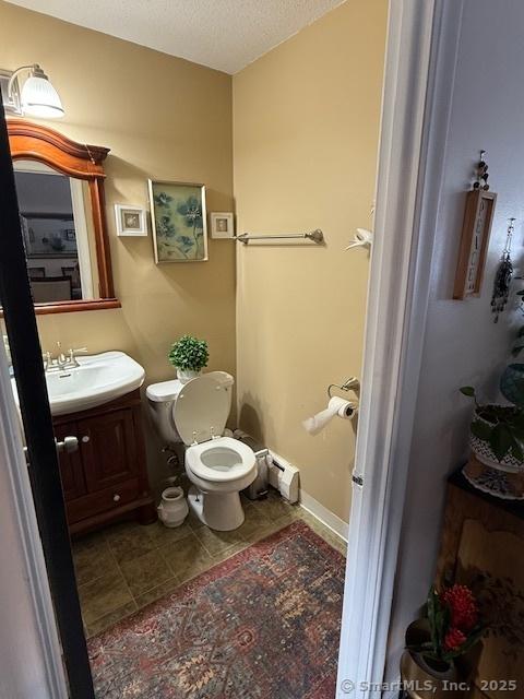 half bath featuring toilet, tile patterned flooring, baseboard heating, a textured ceiling, and vanity