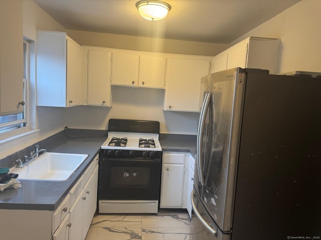 kitchen with stainless steel refrigerator, gas range, white cabinetry, and sink