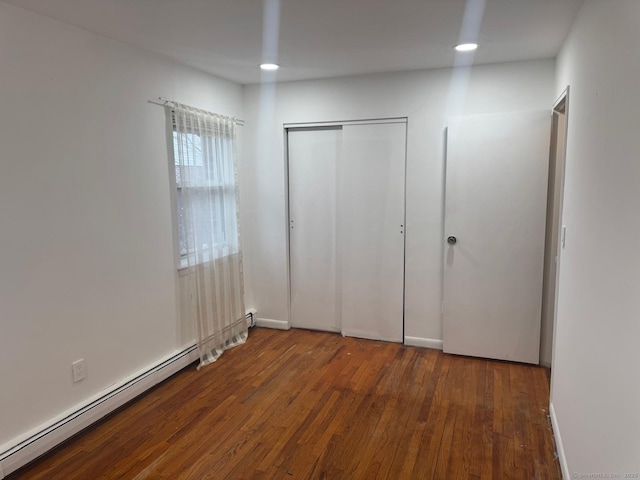 unfurnished bedroom featuring baseboard heating, a closet, and dark wood-type flooring