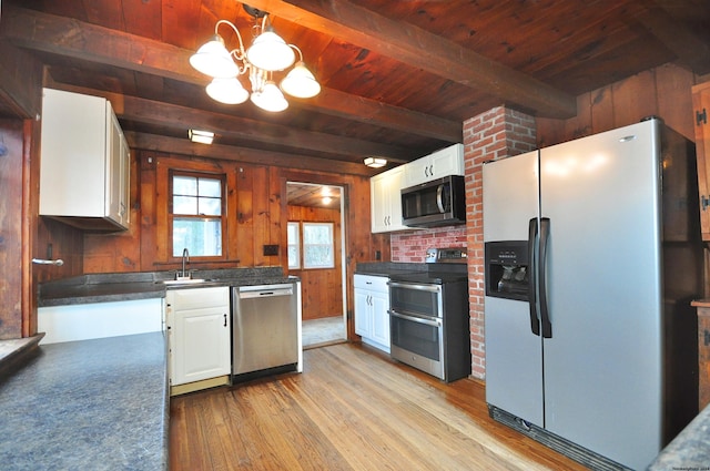 kitchen featuring beam ceiling, white cabinetry, wood walls, decorative light fixtures, and appliances with stainless steel finishes