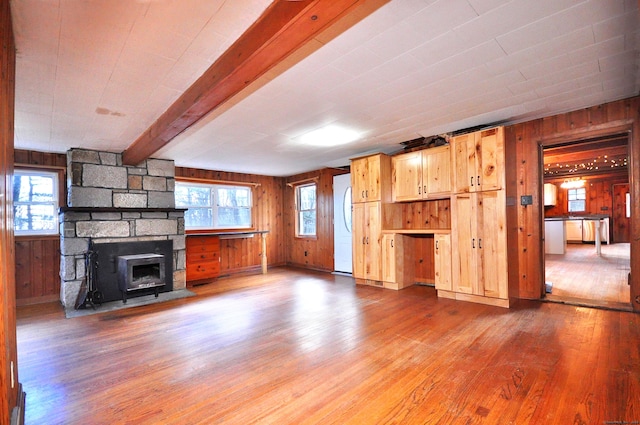 unfurnished living room with beam ceiling, hardwood / wood-style flooring, a stone fireplace, and wooden walls