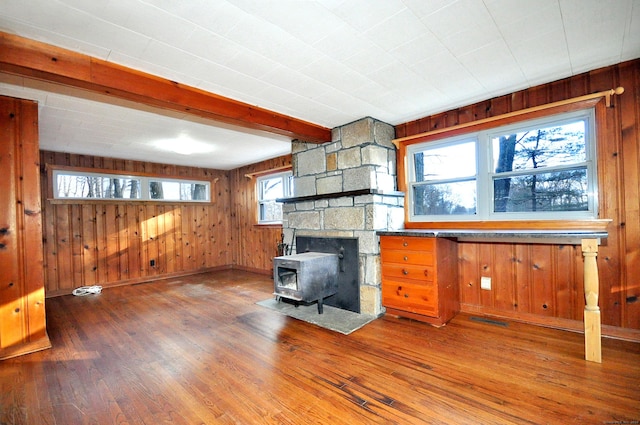 living room featuring beam ceiling, a wood stove, wood walls, and hardwood / wood-style flooring