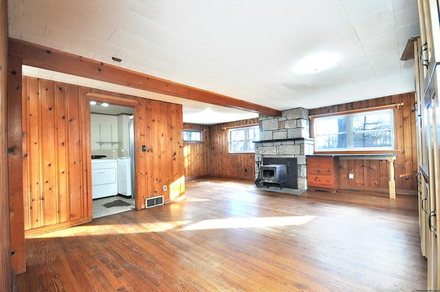 unfurnished living room with beam ceiling, a wood stove, wood walls, washer and dryer, and hardwood / wood-style flooring