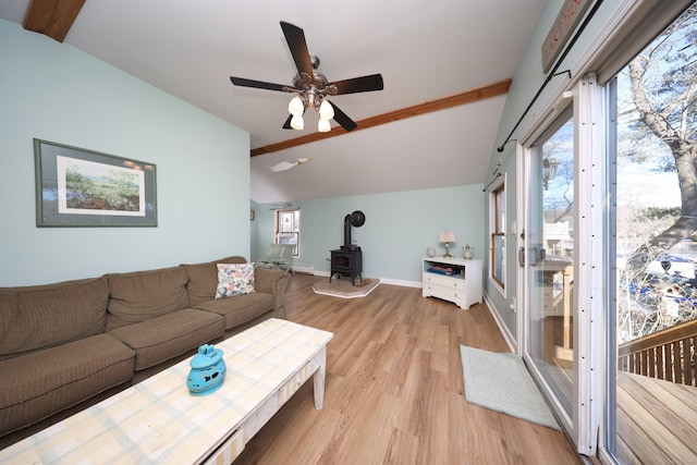 living room with a wood stove, ceiling fan, a wealth of natural light, lofted ceiling, and light wood-type flooring