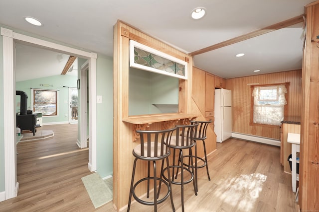 kitchen with lofted ceiling, a wood stove, white refrigerator, baseboard heating, and light hardwood / wood-style floors