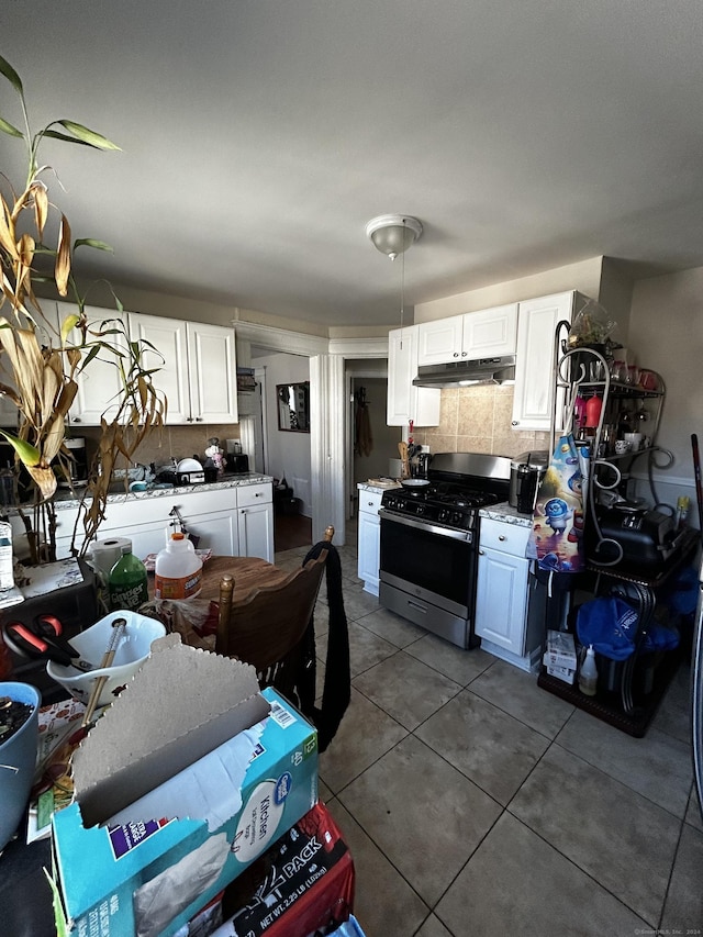 kitchen featuring gas range, decorative backsplash, dark tile patterned floors, and white cabinets