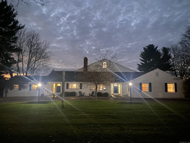 back house at dusk featuring a lawn