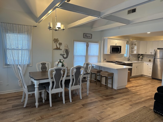 dining space with beamed ceiling, hardwood / wood-style floors, a chandelier, and sink